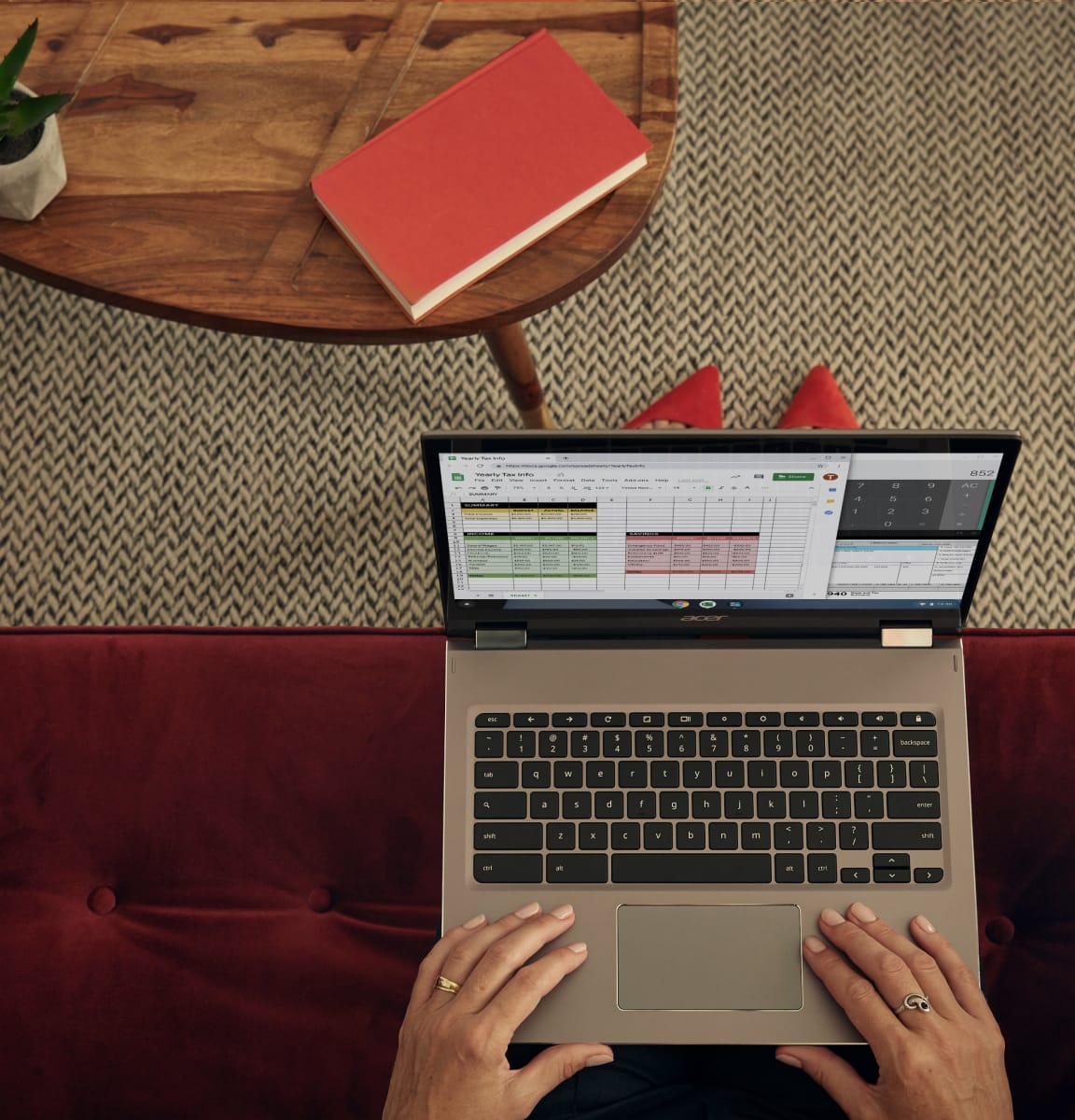 Woman with red shoes works on a Chromebook from a red couch in a hotel lobby.
